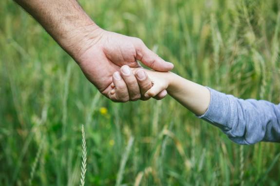 Erwachsene:r hält Kinderhand in Wiese